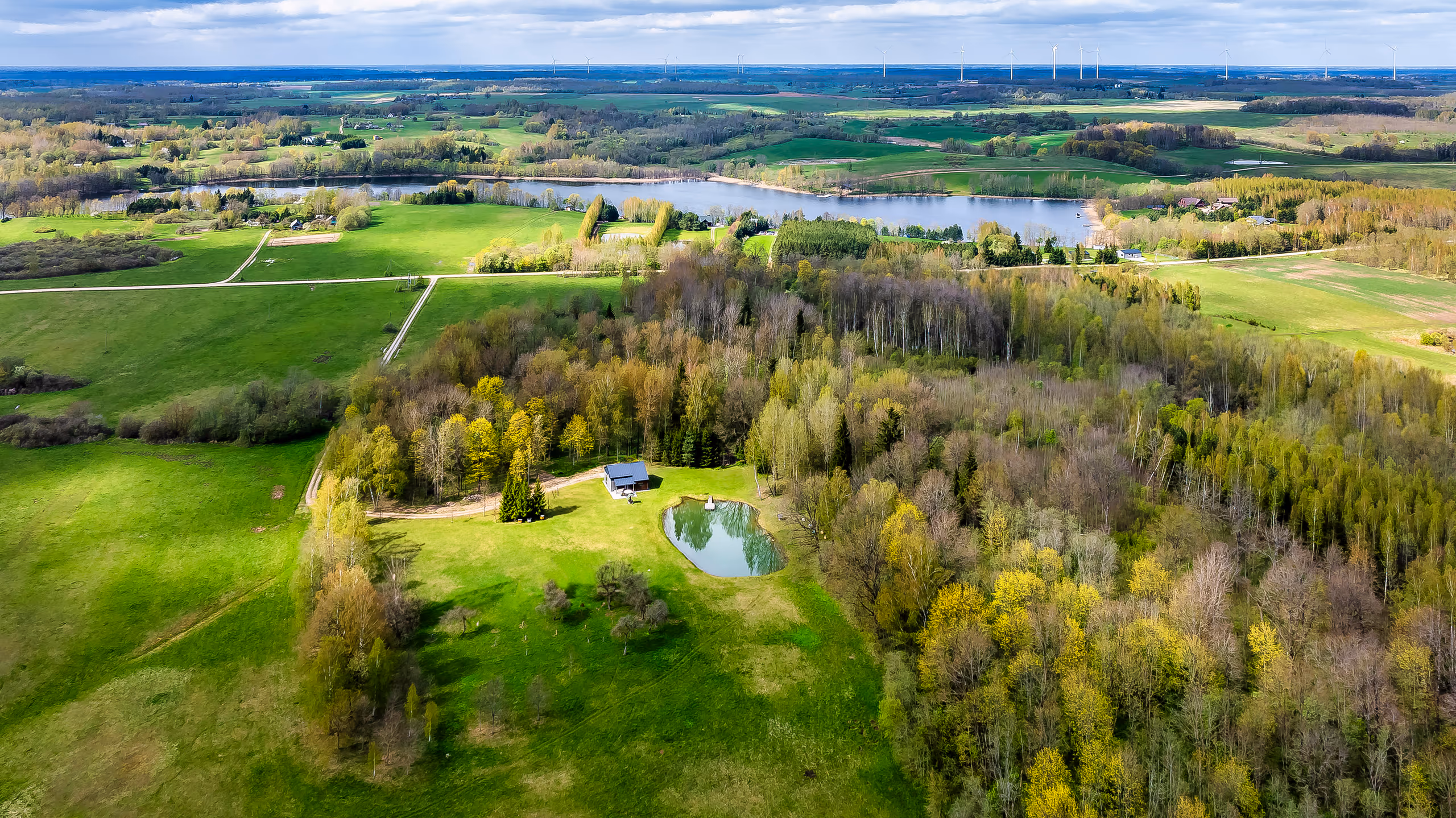 Aerial of Vila Valentino area with Kliepšiai lake on the horizon and wind turbines far in the distance