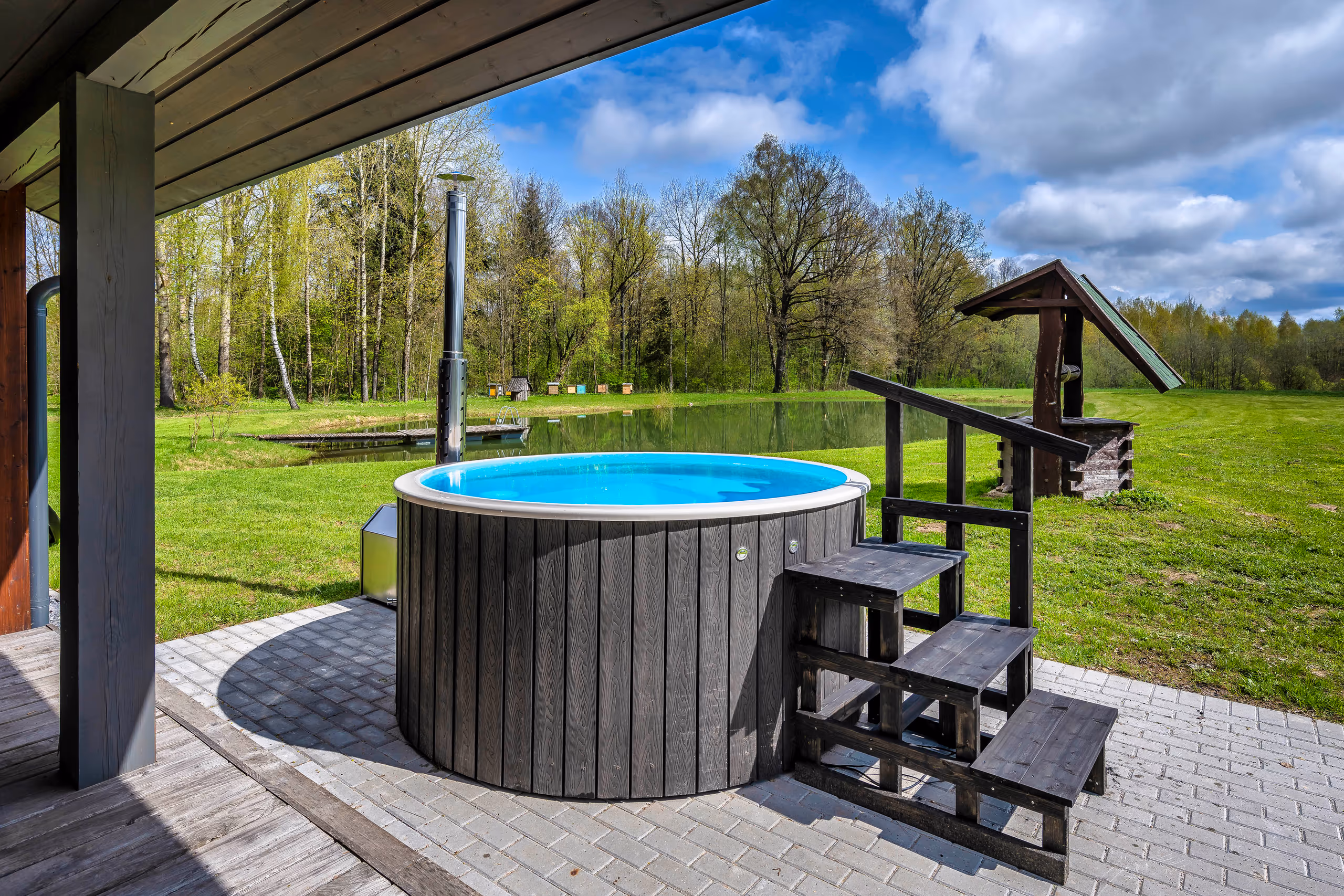 Vila Valentino round wooden hot tub with bright blue water and view to pond and forest